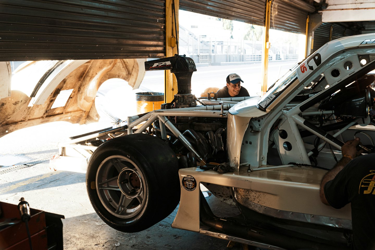 Meccanici che lavorano su un'auto da corsa in un garage con una pista all'esterno.
