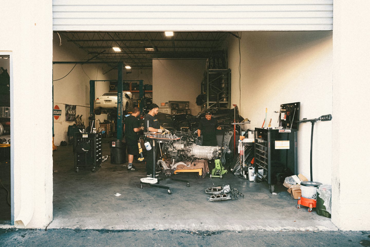 Tre meccanici lavorano insieme su un motore in un'officina.